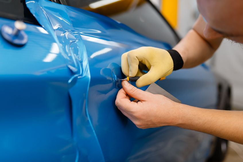 Blue vinyl wrap being applied to the side of a car by a man with one glove