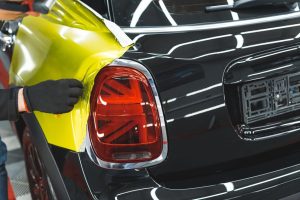 Yellow vinyl wrap being applied to the side of a black car near the tail light